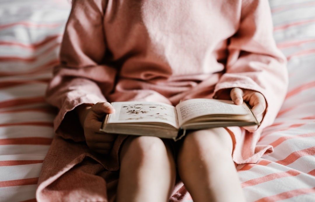 Barn i rosa morgonrock läser en illustrerad bok i sängen