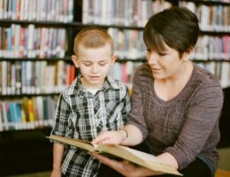 Vuxen läser en bok tillsammans med ett barn i ett bibliotek