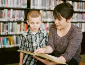 Vuxen läser en bok tillsammans med ett barn i ett bibliotek